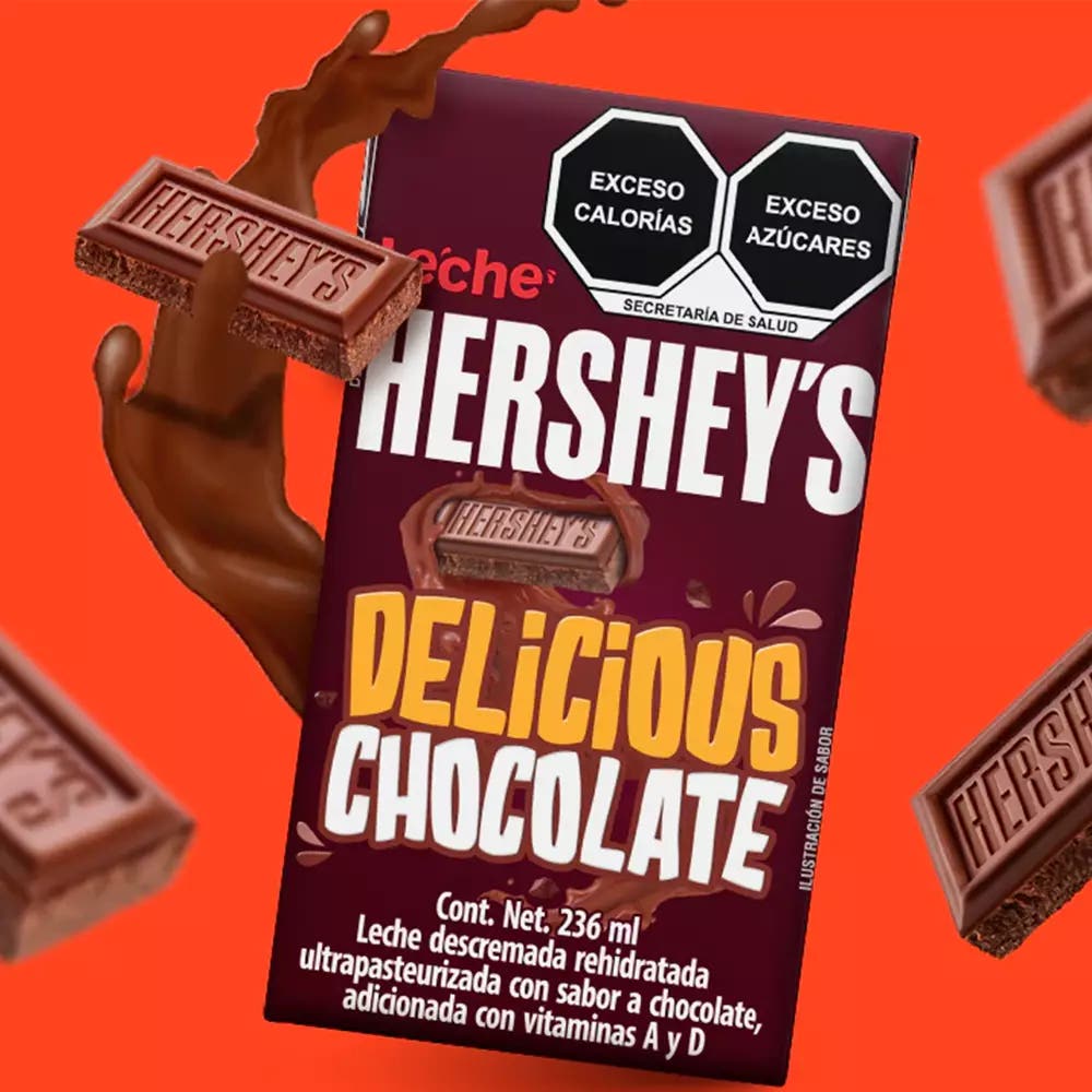 Leche HERSHEY'S sabor Chocolate flotando sobre fondo rojo con un splash de fondo y cuadritos de HERSHEY'S