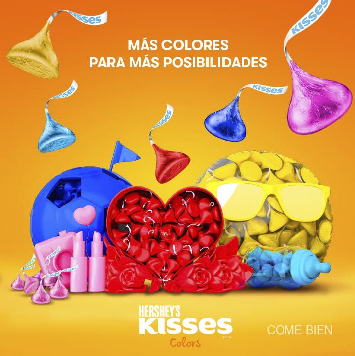 Festejo de KISSES con caja de corazón con rosas, balón de fútbol, lápiz labial y biberón todos con sus KISSES de colores rojo, azul marino, azul cielo, rosa y amarillo sobre fondo rosa amarillo con degradado naranja.
