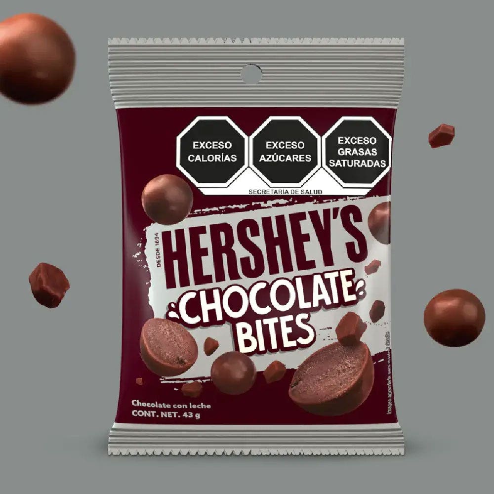 HERSHEY'S Bites Chocolate con Leche 43 g sobre un fondo color gris. Sobre el fondo se observan trozos de chocolate y HERSHEY'S Bites Chocolate con Leche. 